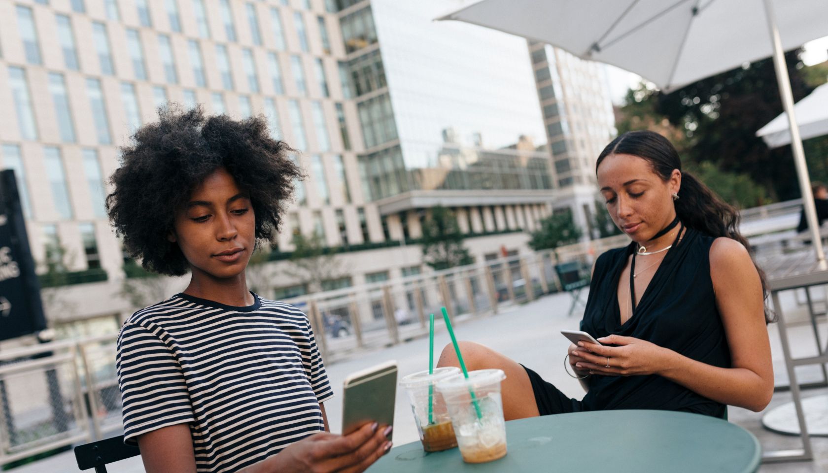 Two friends sitting at pavement cafe looking at their cell phones