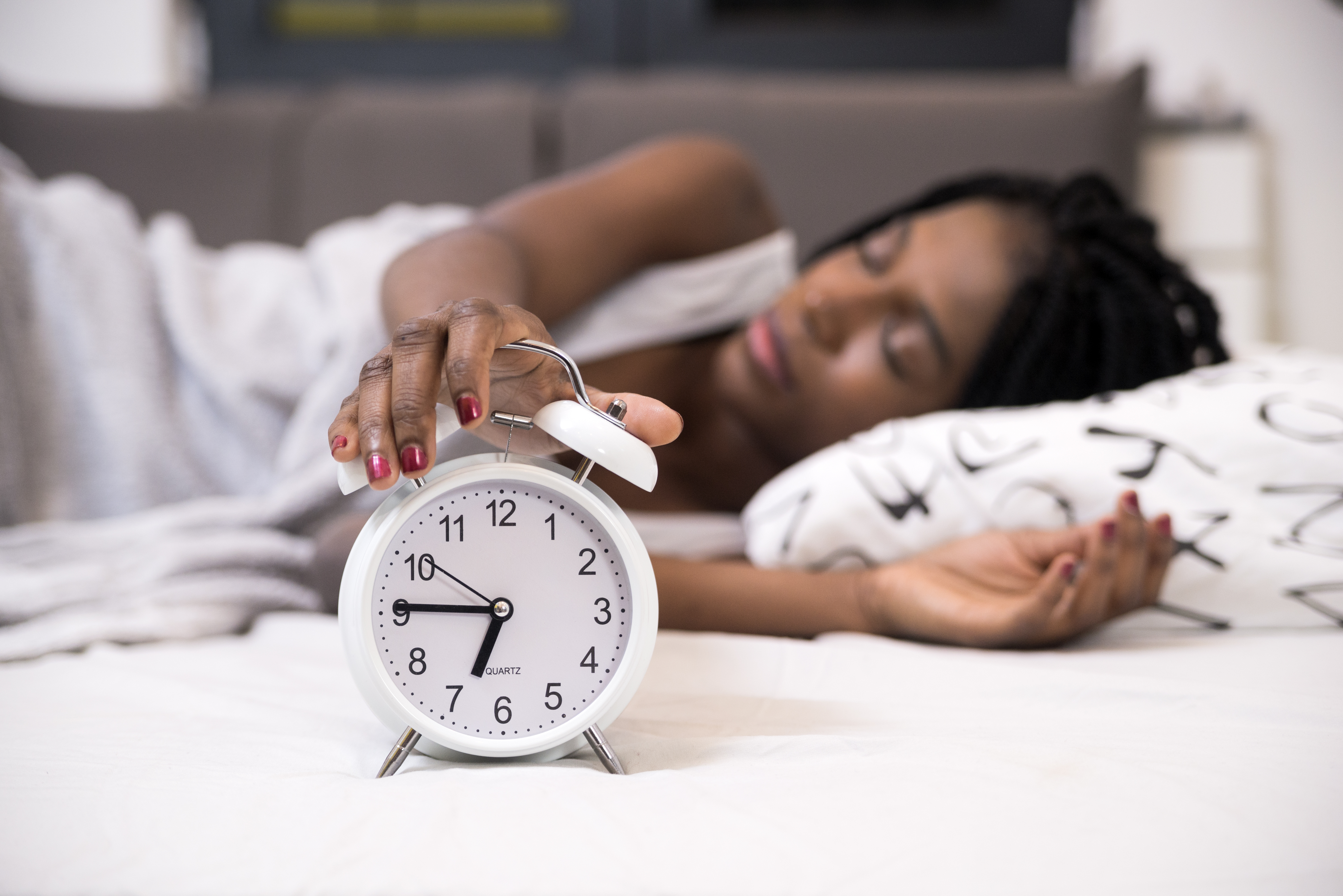 Tired woman switching off her alarm clock in her bedroom