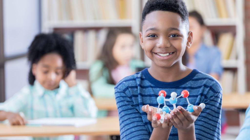 Preteen boy holds a molecular structure model for camera